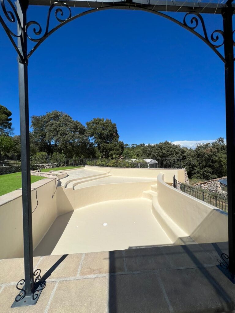 Piscine béton avec revêtement polyester couleur sable sous une pergola